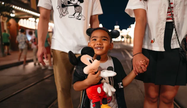 A little girl holds a Mickey Mouse teddy bear while holding her mother's hand in Magic Kindom