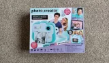 The Photo Creator Instant Camera box, featuring images of the blue and white camera and various smiling people in various poses