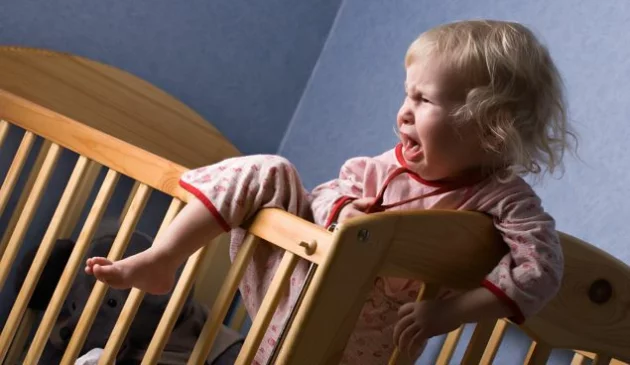 toddler sleep regression image: a little girl tries to climb out of her cot