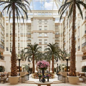 a glass-roofed hotel lobby with towering palm trees