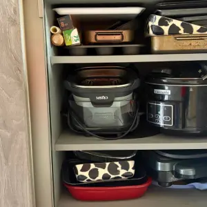 Kitchen cupboard storage with Ninja CRiSPi air fryer, pressure cooker, and various cooking appliances organized on shelves