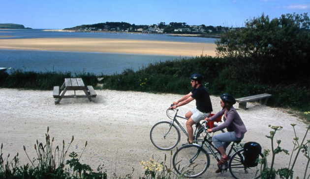 two people cycling next to a sandy beach