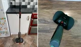 Two images side-by-side show the full length of the black and red electric soray mop being charged in a kitchen with brown vinyl flooring, white cupborads and a red oven. The second photo shows a close up of the black floor head spraying water on the same brown vinyl flooring