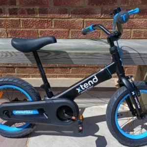 smarTrike Xtend 3-Stage Bicycle with pedals attached leaning against a wooden bench