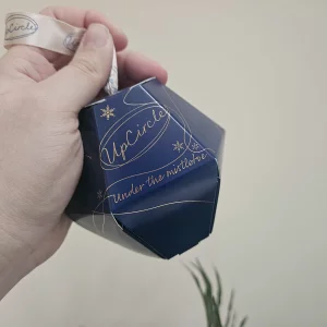 UpCircle Lip Balm Under the Mistletoe stocking filler gift being held by Mumsnet editor Rebecca against a wall