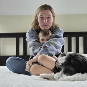 Mumsnet editor Rebecca holds her child atop a mattress during testing, they're joined by the dog