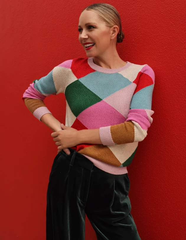 A model wearing Boden's Sparkly Argyle Jumper against a red background