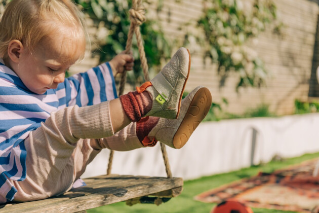 A toddler sits in a swing with their legs in the air wearing Brightland shoes
