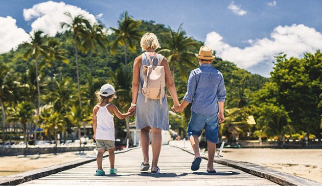 a mum holding hands with two children, walking down a jetty in a hot country