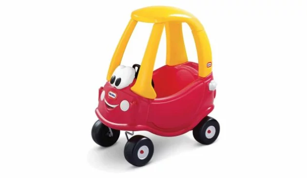 A Cozy Coupe ride-on car. It has four large black wheels, a red body and yellow roof. A large pair of eyes sit at the front of the car.