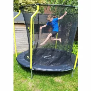 A girl in a blue top and black shorts bouncing on a black and yellow Plum trampoline