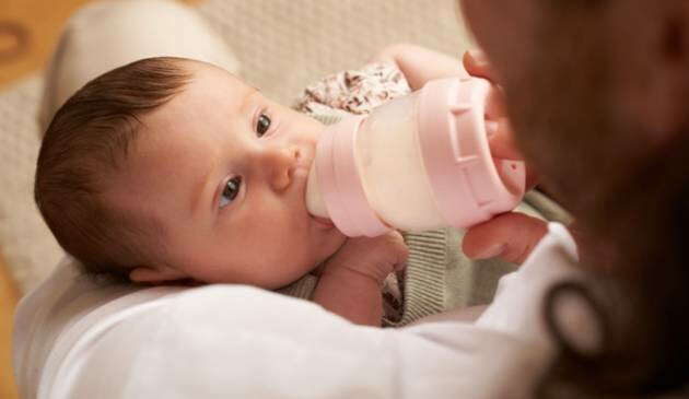 A baby looking at their mother while being fed