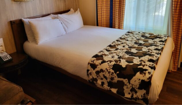 A double bed with white sheets and pillows and a cow print throw