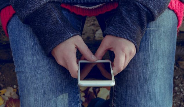 A close up of a pair of woman's hands holding a smartphone in her lap