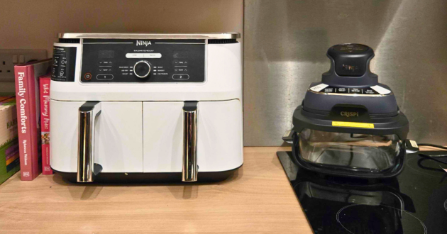 Ninja kitchen appliances including dual zone air fryer and CRiSPi system with cookbooks on wooden counter