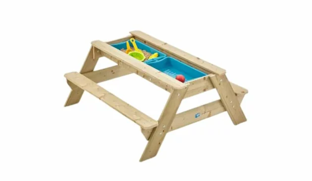 A wooden picnic table with two blue plastic trays set in the middle. One tray contains sand and yellow plastic sand play toys