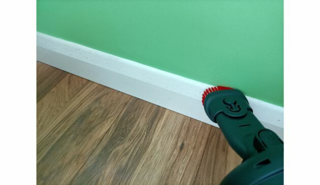The 2-in-1 Henry Quick combi tool being used to hoover a white skirting board, sitting below a lime green wall and wood-effect floor