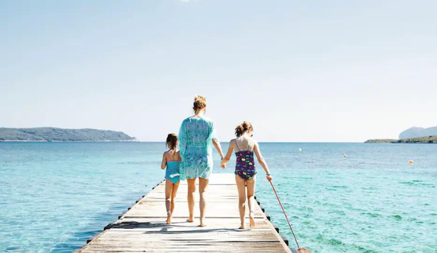 a mum holding hands with two children walking along a jetty, surrounded by turquoise sea
