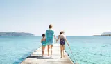 a mum holding hands with two children walking along a jetty, surrounded by turquoise sea