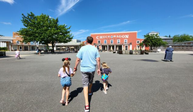 A man hand in hand with two children walking in a courtyard towards a red building