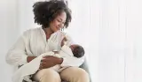 A mother holds her baby in her arms while she's sat down, she's smiling at the baby