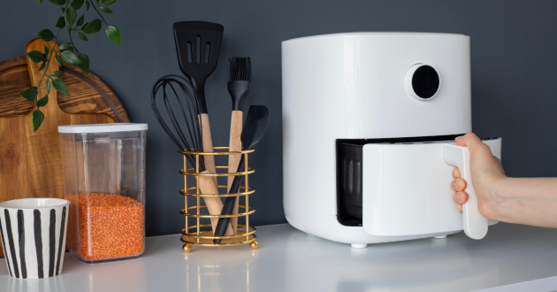Air fryer on a kitchen counter-top, hand removing the basket