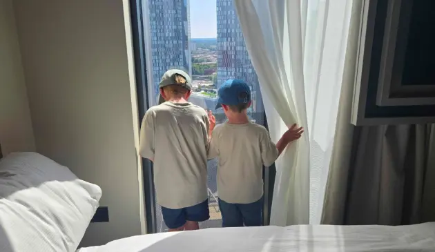Two young children look out of the window from the Aloft Manchester hotel