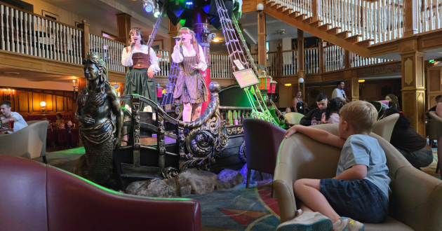 Two singers performing in the Alton Towers Hotel Atrium as a child watches from nearby seating