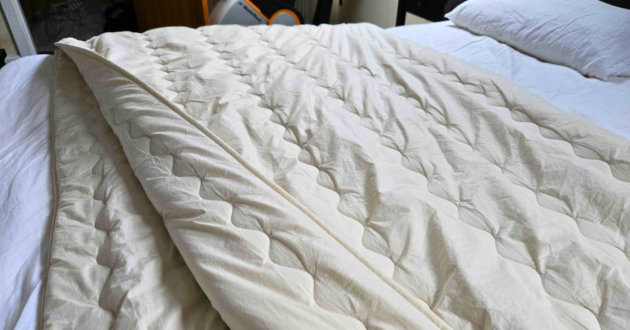 Ava Innes Year Round 8–11 tog duvet folded back on a super king bed, showing the dense, naturally weighted fill and organic cotton cover