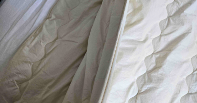 Detail of the Ava Innes duvet layered over bedding, highlighting the organic cotton casing and structured stitched quilting