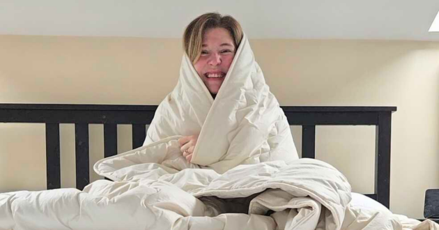 Reviewer wrapped in the Ava Innes Cashmere and Wool Duvet on a super king bed, demonstrating the naturally weighted cocooning feel