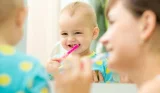 Baby brushing teeth with help from parent