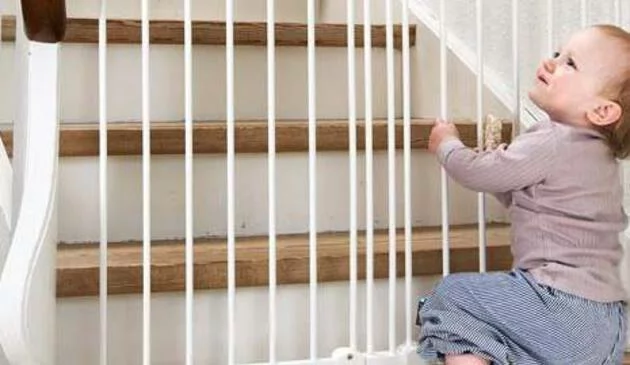 Toddler holding on to stair gate at bottom of stairs