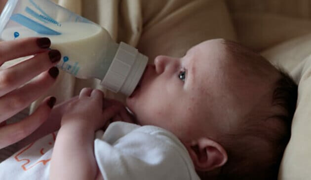 profile of baby head and shoulders while being fed by a bottle