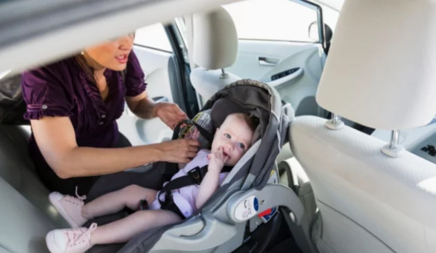 Baby being strapped into car seat by woman