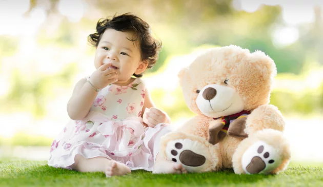 Baby girl sat on grass with teddy