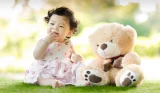 Baby girl sat on grass with teddy
