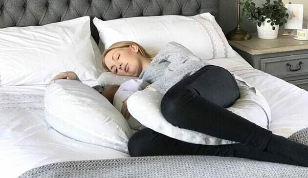 Pregnant woman lying on bed using full moon pillow