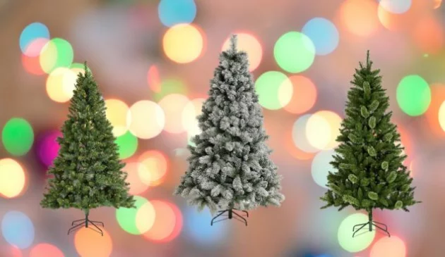 Three artificial Christmas trees on a blurred background of multi-coloured lights. The tree in the middle of the three is covered in fake snow. The other two are green.