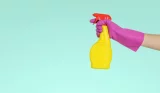 hand wearing pink maigolds holding yellow spray bottle with red lid