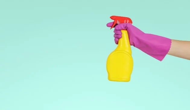 hand wearing pink maigolds holding yellow spray bottle with red lid