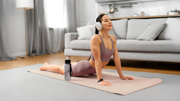 A woman is doing yoga on a yoga mat with headphones on