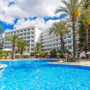 two people playing catch in a swimming pool in front of a large hotel