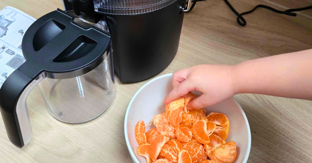 Child adding peeled orange segments into Braun MultiJuice 5 juicer next to juice jug and instruction manual