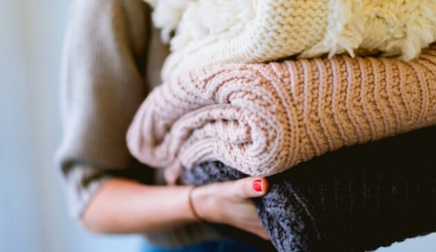 A close-up of a woman with red-painted nails carrying a pile of thick woollen items coloured white, pink and black