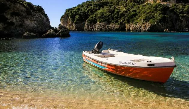A picture of a boat beached on the sand. Behind it is sea and hills.