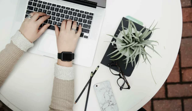 Woman typing on a laptop with a desk plant