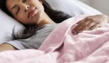 A woman sleeps in bed with a Cosi Home heated throw over her