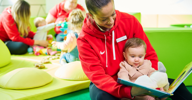 Three young children sitting at a table doing arts and crafts with paper, pens and play materials in a supervised kids’ activity space