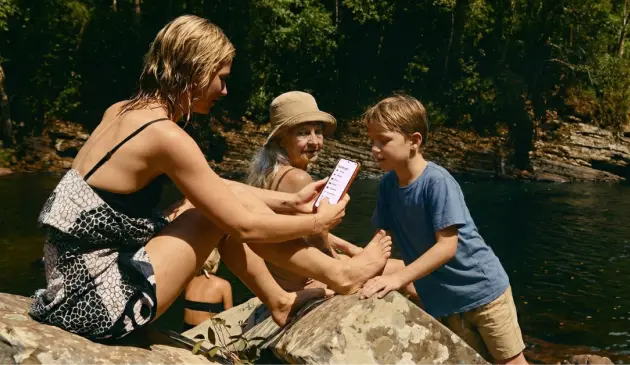 Mother, grandmother and boy using smartphone by a lake